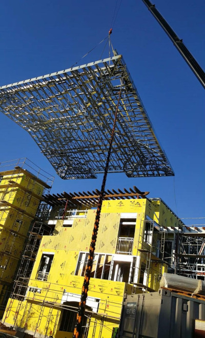 Superior Wall Systems construction site with a large roof section being moved into place with a crane.