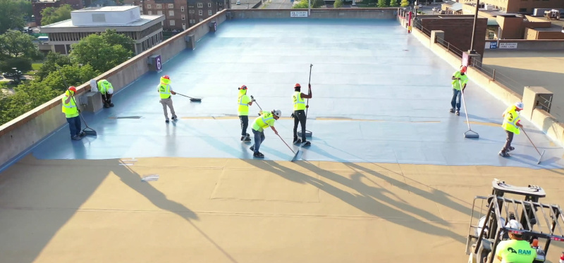 RAM Construction Services applying product on a rooftop with a group of men working.